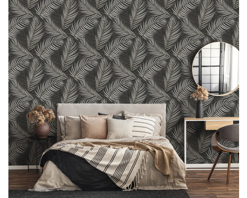 Schlafzimmer mit Bett vor einer Wand mit Blättermuster Tapete.