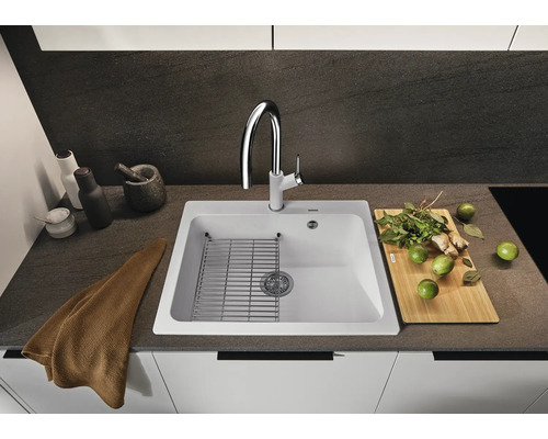 Küchenspüle mit Abtropfgitter, Armatur, Schneidebrett und Kräutern auf einer Küchentheke.