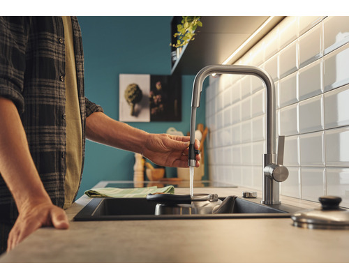 Eine Person bedient einen Küchenarmatur mit Wasserauslauf in einer modern gestalteten Küche.