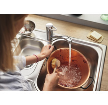Frau spült Kupfertopf in einer Edelstahlspüle mit Wasserhahn.
