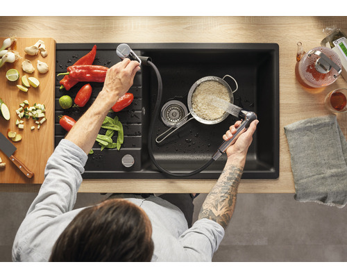 Aufnahme von oben einer Spüle mit Abtropffläche und einer Person, die Reis mit einem Wasserhahn abspült, neben dem sich Gemüse befindet