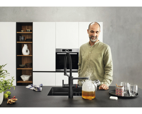 Moderne Küche mit schwarzer Armatur, Spüle und einem Mann, der einen Glaskrug mit heißem Wasser betrachtet.