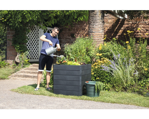 Mann gießt Pflanzen in einem Pflanzkasten im Garten.