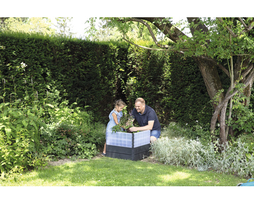Vater und Tochter arbeiten gemeinsam an einem Hochbeet im Garten.