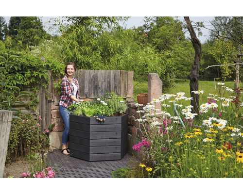 Frau steht neben einem Hochbeet aus Holz im Garten.