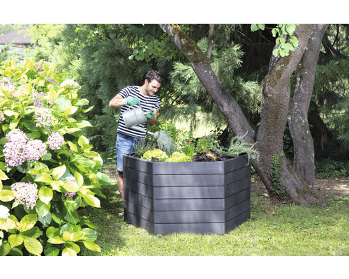 Mann gießt Pflanzen in einem Hochbeet im Garten.