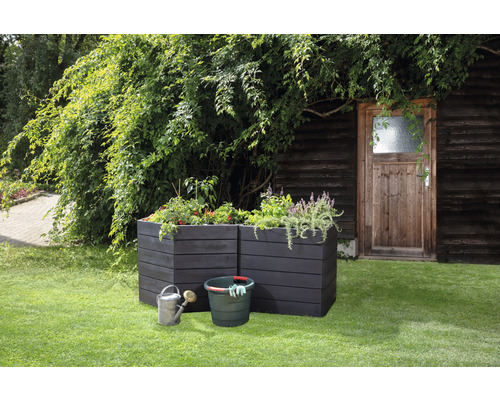 Szene mit zwei Hochbeeten aus Holz, einem Eimer, einer Gießkanne und Pflanzen im Garten