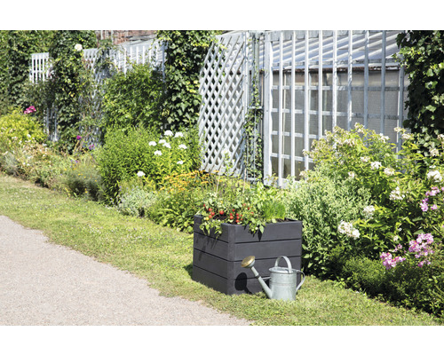 Gartenszene mit bepflanztem Hochbeet und Gießkanne vor einem Gartenzaun