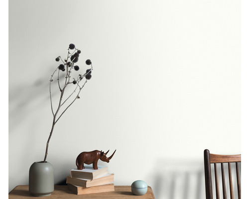 Wohnraum mit Arrangement aus Vase, Dekorationsobjekt und Bücherstapel vor einer gestrichenen Wand.