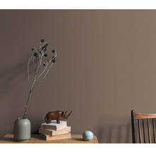 Nahaufnahme einer braunen Wand mit Textiltapete, dekoriert mit einer Vase, einer Holzfigur und Büchern