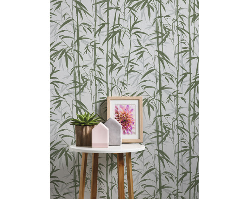 Nahaufnahme einer Wand mit Bambustapete, einem kleinen Tisch, einer Zimmerpflanze, Deko-Häusern und einem Bilderrahmen
