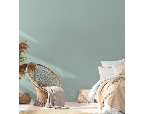 Helles Schlafzimmer mit Korbsessel, Bett und Trockenblumen