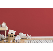 Kinderzimmer mit Nachttisch, Spielzeug und Teppich vor roter Wand