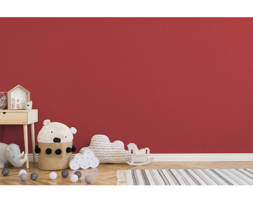 Kinderzimmer mit Nachttisch, Spielzeug und Teppich vor roter Wand