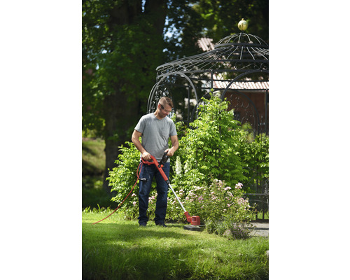 Ein Mann benutzt einen Rasentrimmer im Garten, im Hintergrund ein Pavillon.