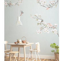 Esszimmer mit hellem Holztisch, Stühlen, Hocker, Geschirr, Zimmerpflanze und einer Wandtapete mit Vogel- und Blütenmotiven.