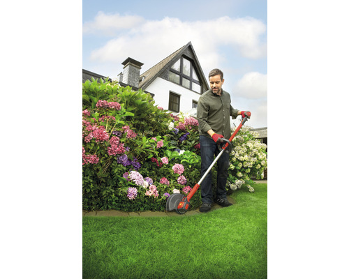 Mann trimmt Rasen mit Rasentrimmer im Garten vor einem Haus