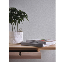 Nahaufnahme einer Wand mit strukturierter Tapete, einem Holztisch mit Schublade, Büchern und einer Topfpflanze