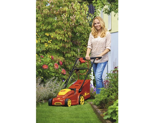 Frau bedient einen roten und gelben Rasenmäher der Marke Wolf Garten auf einem Rasen in einem Garten.