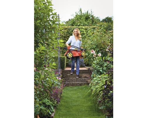 Frau trägt zusammengeklappten Rasenmäher im Garten.