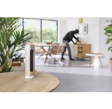 Netatmo Überwachungskamera auf Tisch mit Einbrecher im Hintergrund