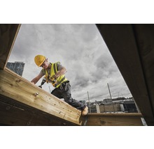 Handwerker mit Bohrmaschine arbeitet auf einer Holzkonstruktion im Freien.