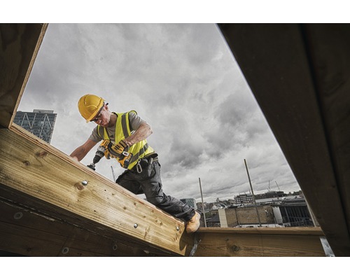 Handwerker mit Bohrmaschine arbeitet auf einer Holzkonstruktion im Freien.