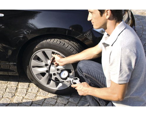 Mann prüft Reifendruck am Auto mit Reifendruckmesser