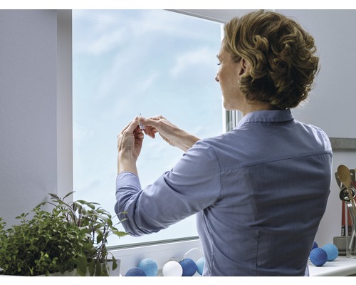 Frau befestigt eine Fensterschutzfolie am Fenster