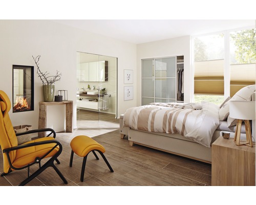 Helles Schlafzimmer mit Bett, Sessel, Kamin und Zugang zum Badezimmer.