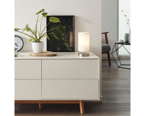 Wohnzimmerszene mit Kommode, Tischleuchte, Zimmerpflanze und Dekoration