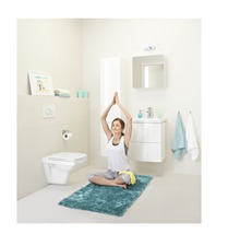 Helles Badezimmer mit Toilette, Waschbecken, Spiegel und einer Frau beim Yoga auf einem Teppich