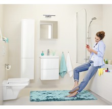 Badezimmer mit Toilette, Waschbecken, Spiegel, Badewanne und einer Frau, die auf dem Badewannenrand sitzt