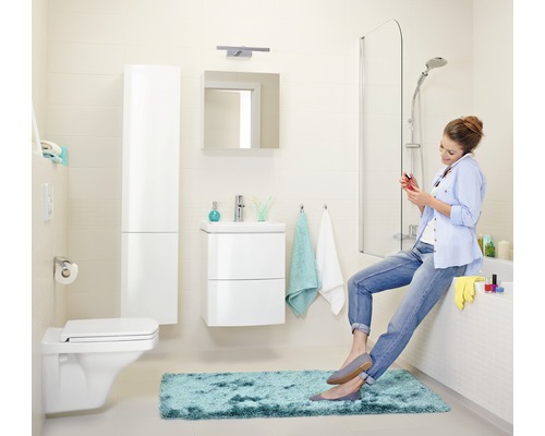 Badezimmer mit Toilette, Waschbecken, Spiegel, Badewanne und einer Frau, die auf dem Badewannenrand sitzt