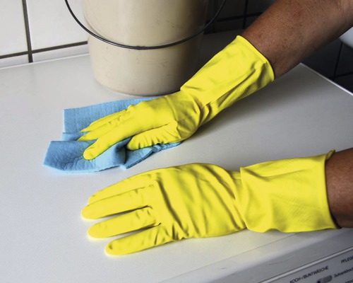 Reinigungskraft mit Gummihandschuhen und Putzlappen reinigt Oberfläche