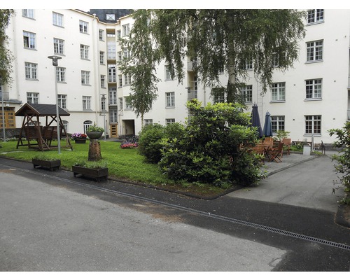 Innenhof mit Schaukel, Blumenbeeten, Bäumen und Sitzgelegenheiten vor einem mehrstöckigen Gebäude.