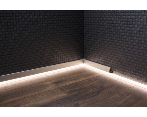 Ecke eines Raumes mit Sockelleisten inklusive indirekter Beleuchtung an einer strukturierten Wand und Holzboden