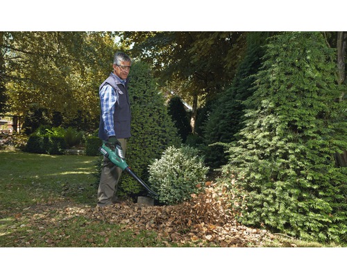 Mann verwendet einen Laubbläser im Garten, um Blätter zu entfernen.