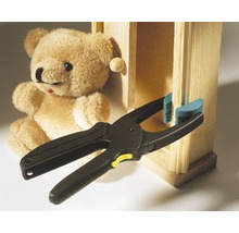 Federzwinge beim Fixieren eines Holzstücks an einem Miniaturschrank, mit einem Teddybär im Hintergrund