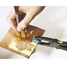 Eine Person graviert eine Rose in eine Metallplatte mit einem Gravierwerkzeug, die Platte wird von einer Klemme gehalten.