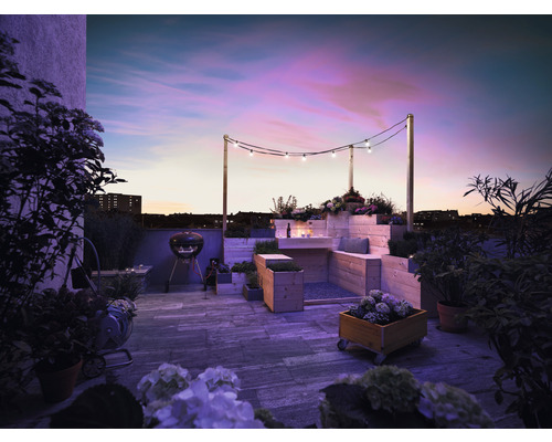 Dachterrasse mit Grill, Holzmöbeln, Bepflanzung und Lichterkette bei Dämmerung