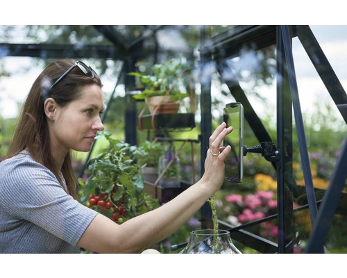 Frau bedient Tablet in einem Gewächshaus, umgeben von Pflanzen
