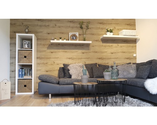 Wohnzimmer mit grauer Couch, Couchtischen, Regalen und Holzdekor an der Wand