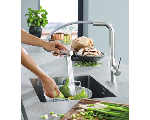 Küchenszene mit Spültischarmatur und Person, die Gemüse wäscht