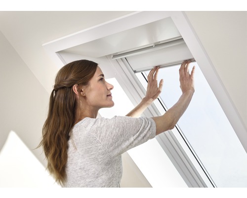 Eine Frau bedient ein Dachfenster in einem hellen Raum.