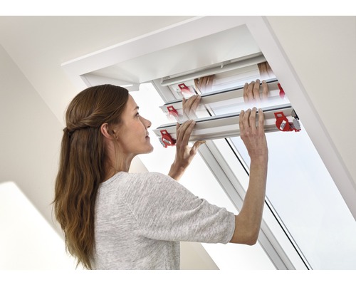 Frau bedient ein Dachfenster mit einem Rollladen zur Verdunkelung.