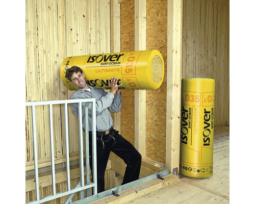 Mann trägt eine Rolle Isover Dämmwolle. Eine weitere Rolle Isover Dämmwolle steht im Raum.