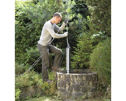 Mann installiert eine Tiefbrunnenpumpe in einem Brunnen im Garten.