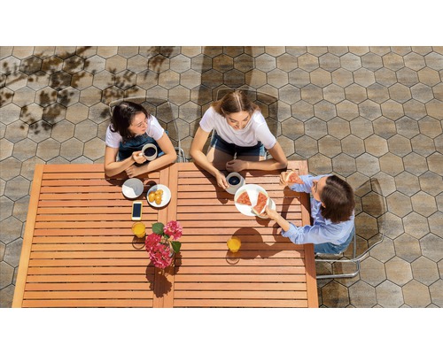 Drei Frauen sitzen an einem Holztisch im Freien und essen Pizza und Gebäck.