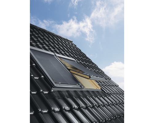 Dachfenster mit Sonnenschutzrollos auf einem Ziegeldach vor blauem Himmel